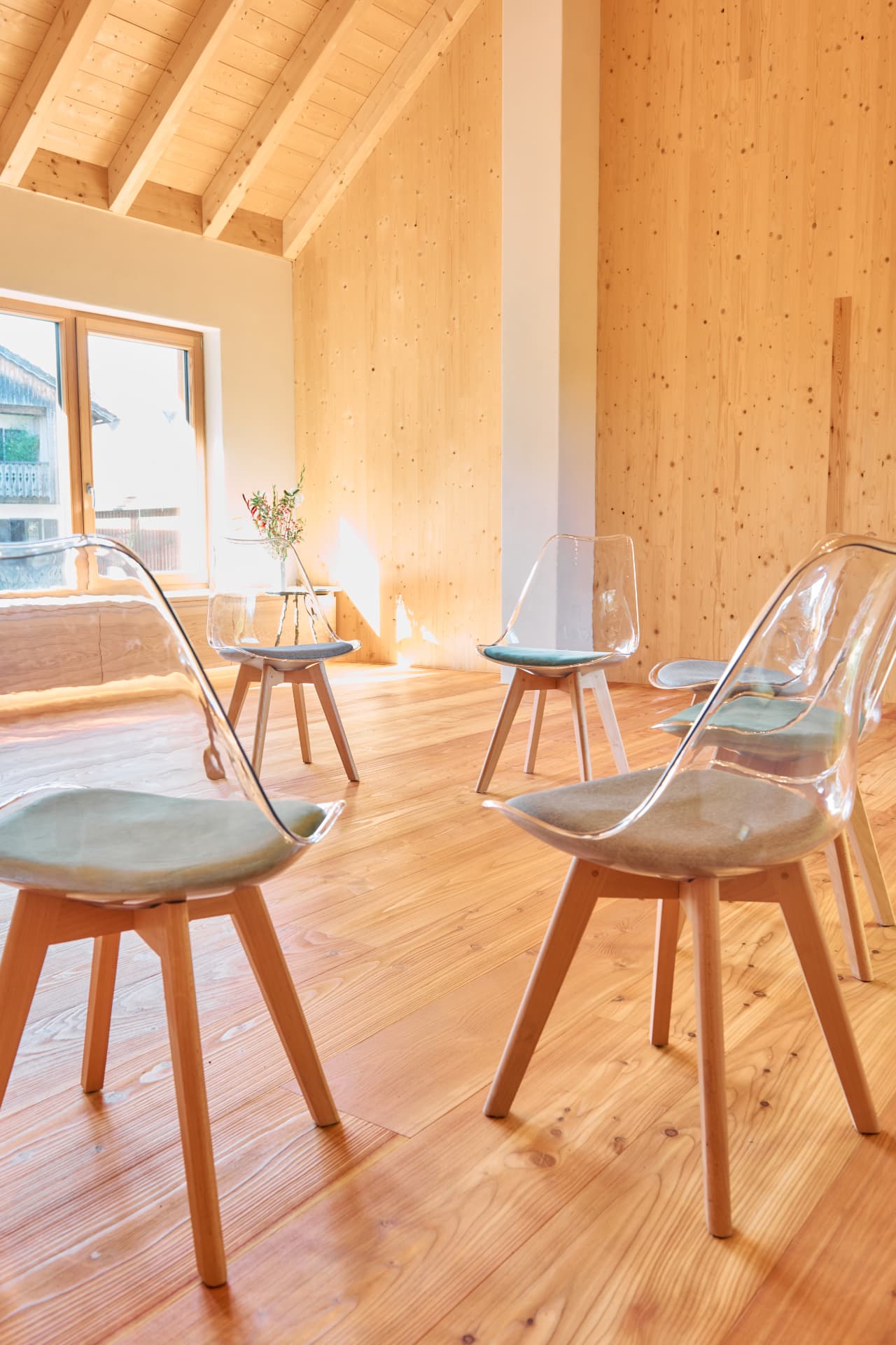 Stuhlkreis aus transparenten Stühlen im lichten Holzraum