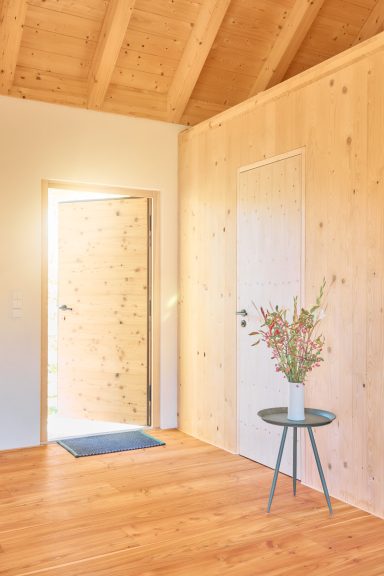 Heller Eingangsbereich mit Holzwänden, offener Tür und Tisch mit einer Blumenvase.
